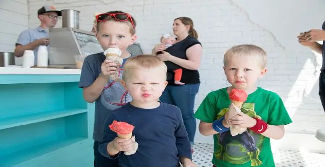 A group of kids eating ice cream in front of a wall.