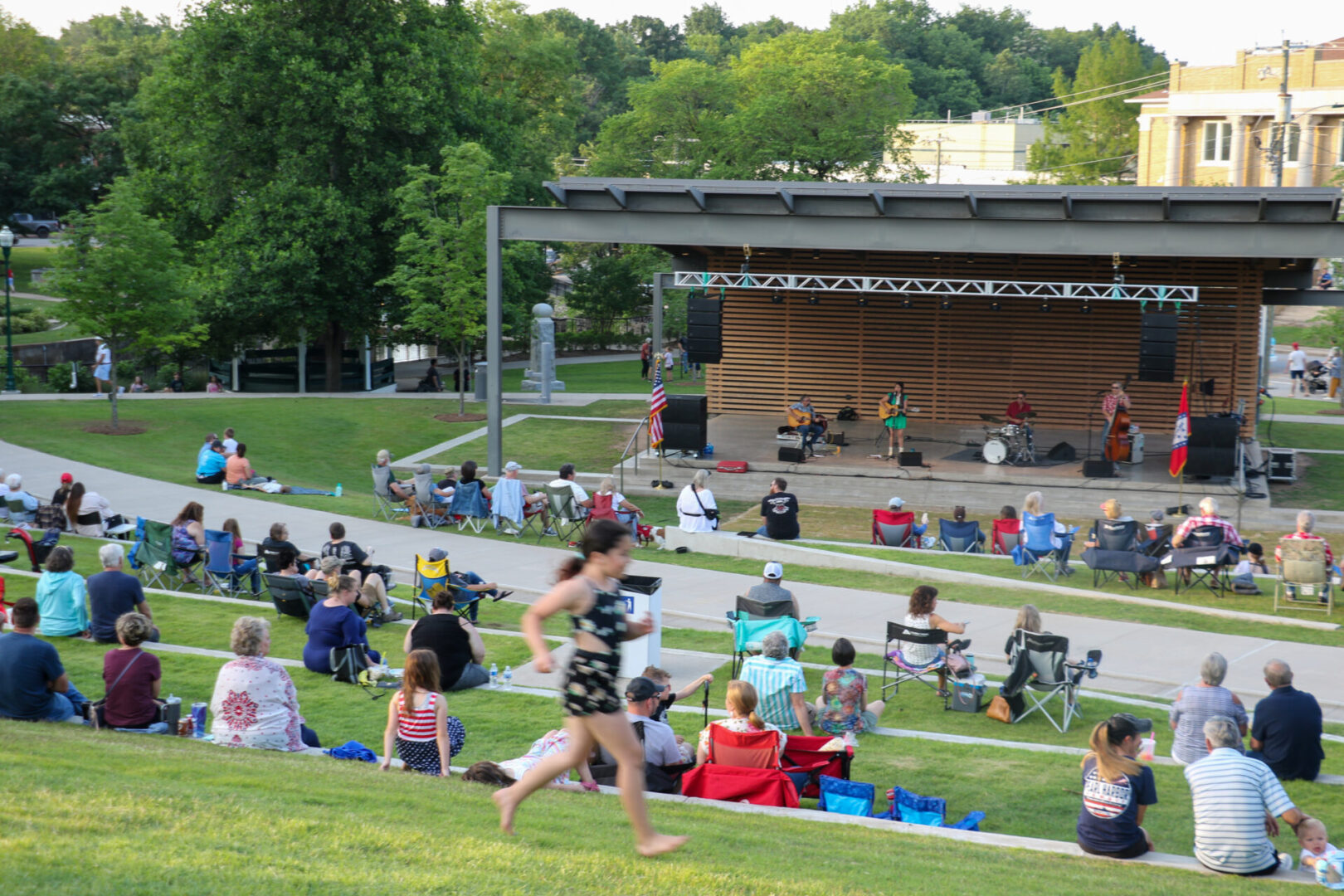 A crowd of people sitting on the grass in front of an amphitheater.